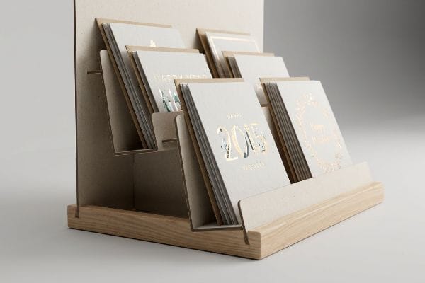 Light wood and cardboard tiered retail display showcasing foil-stamped Happy New Year greeting cards with gold accents.
