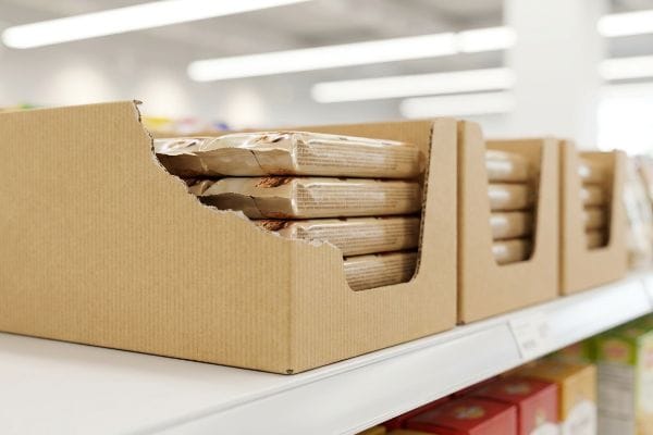 Retail shelf displays brown cardboard shelf-ready packaging (SRP) boxes with stacked products visible through a torn opening.