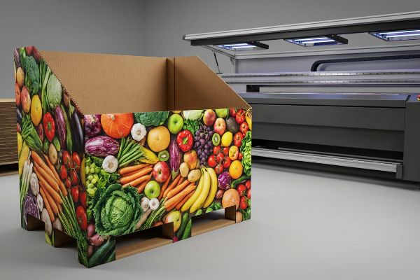 Vibrant UV-printed corrugated merchandiser showcasing fresh produce, next to a large flatbed digital printer.