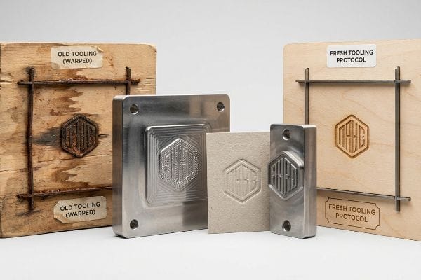 Old warped plywood tooling and fresh laser-cut tooling with precision metal dies, demonstrating an embossed AHS logo on paper.