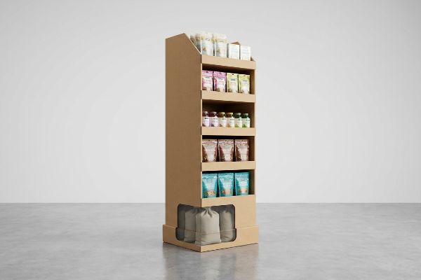 Brown corrugated cardboard freestanding display with five shelves of diverse products and a weighted false bottom showing sandbags for stability.