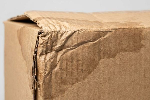Wet Corrugated Cardboard Damage Moisture-damaged brown corrugated cardboard box with warped, wrinkled flaps and dark water stains, illustrating humidity absorption.