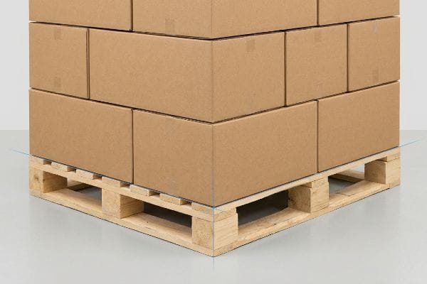 茶色の段ボール箱が、はみ出しがないように木製パレットに積み重ねられ、角がぴったり合うように透明なラップで固定されている。.