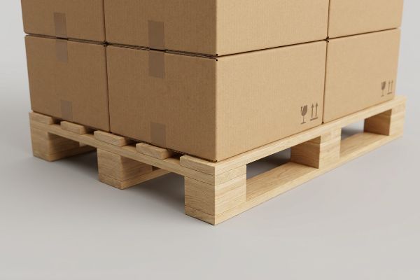Light wooden pallet supporting stacked brown cardboard boxes with fragile symbols, illustrating zero-overhang for secure shipping.