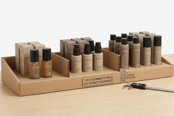 Corrugated cardboard display with BRMONC cosmetic bottles, illustrating the 3-5-7 Asymmetry Rule and 0.25-inch (6.35 mm) clearance measured by a digital caliper.