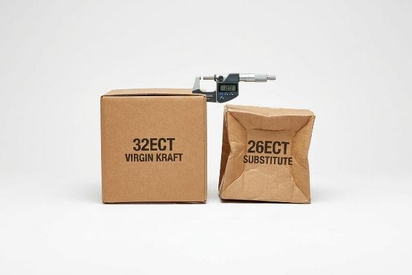A rigid 32ECT Virgin Kraft box stands beside a crumpled 26ECT Substitute, with a digital micrometer comparing their structural integrity.