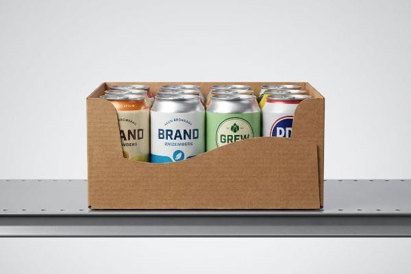 Corrugated PDQ retail tray with die-cut swooping front lip, displaying six beverage cans with 85% label visibility, including 'Brand' and 'Grew', on a metal shelf.