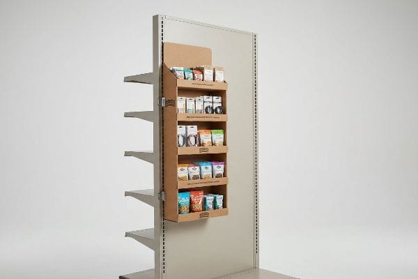 Attached to a gray retail shelving unit, a cardboard sidekick display showcases various impulse snack products in small pouches.