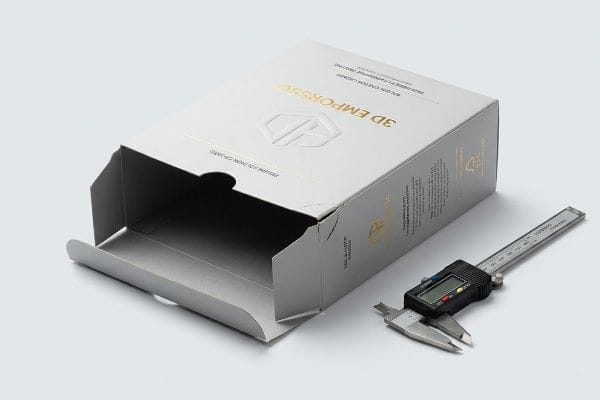 Light grey carton board box, open and empty, displays '3D Emposso' branding and 'Premium Folding Carton' text, positioned next to a digital caliper for precise measurement.