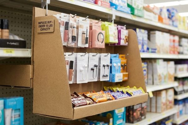 Power Wing Impulse Display A retail corrugated power wing display, labeled 'Impulse Buy - Under 15 Lbs Capacity,' holds cosmetics, earbuds, and candy bars.