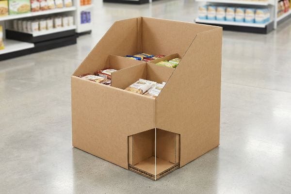 段ボール製ゴミ箱ディスプレイ 小売店の通路には、茶色の段ボール製のダンプビン型陳列棚が設置されており、内部の仕切りで様々な包装済みスナック菓子が収納され、二重構造の底面が際立っている。.