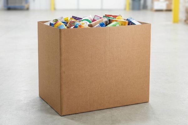 Brown corrugated cardboard dump bin display, overflowing with assorted packaged consumer goods, on a concrete warehouse floor.