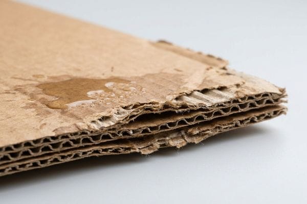 Swollen Corrugated Cardboard Brown corrugated cardboard with visible water damage, showing wet spots, swollen, and frayed edges revealing the internal flutes.