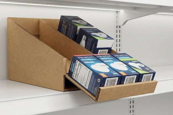 A retail shelf displays a corrugated cardboard gravity feed rack, automatically dispensing blue and green Healxton product boxes with visible Nutrition Facts.