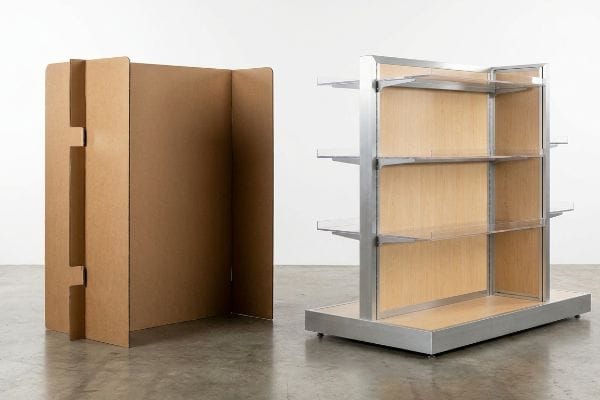 POP Display Types Compared Side-by-side, a semi-permanent corrugated cardboard display stands next to a permanent metal and wood retail shelving unit with acrylic fronts.