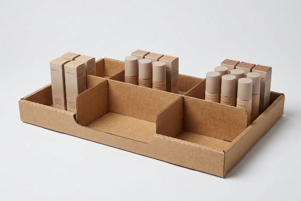 Brown corrugated cardboard display tray with modular dividers organizes cosmetic bottles and boxes for retail product merchandising.