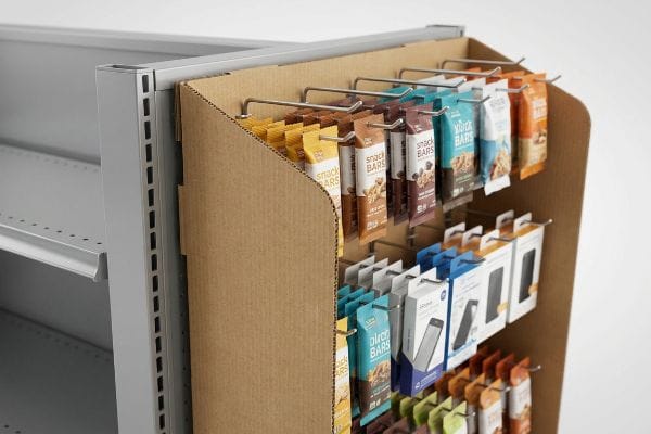 Corrugated cardboard power wing display featuring Snack Bars and small electronics on metal hooks, attached to a gray retail shelving unit.