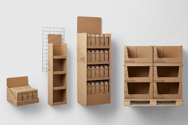 Various corrugated cardboard PDQ displays: a filled countertop tray, two floor standees, and empty pallet bins on a wooden pallet.