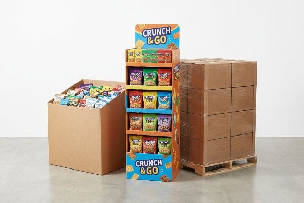 A retail setting features a Crunch & Go POP floor display, a dump bin with assorted snacks, and a quarter-pallet shipper with brown boxes.