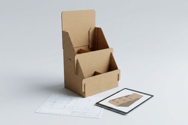 Cardboard POP Display Design Brown corrugated cardboard point-of-purchase display with design blueprint and tablet showing 3D rendering.