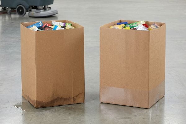Corrugated dump bins, one with water-damaged raw testliner base from floor moisture, beside another protected by a clear poly-coat mop guard, both filled with retail products.