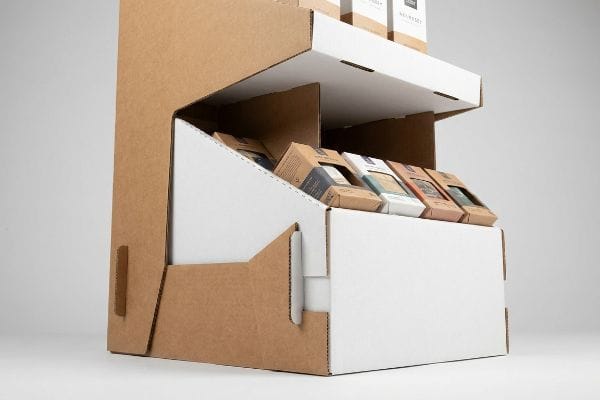 Custom Cardboard Display Angled custom cardboard display, crafted from corrugated board and white paperboard, presenting diverse small retail product boxes on a gravity-feed shelf.