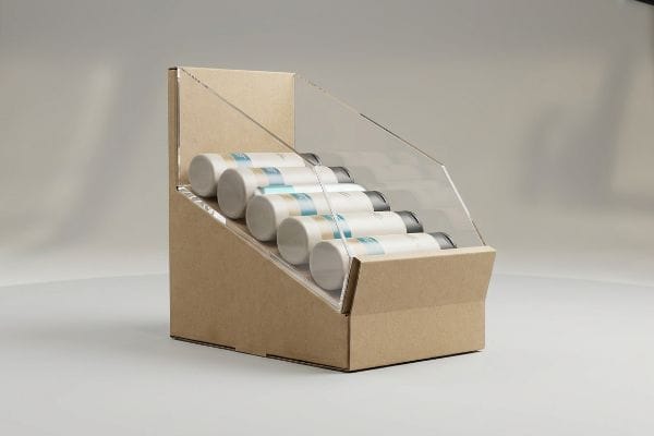 Gravity Feed Display Bottles Six white cylindrical bottles are displayed in a kraft cardboard gravity feed merchandising unit with a clear acrylic front panel.
