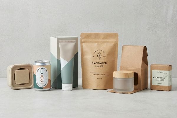 Une collection de produits de grande consommation dotés d'emballages écologiques, comprenant une canette Uac, un sachet de snacks emballés et un pain de savon cosmétique.
