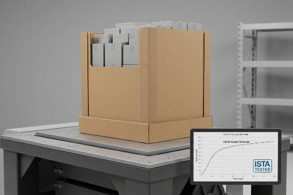 Corrugated cardboard retail display box filled with gray packages on an ISTA vibration testing table, showing a 150-lb Kinetic Threshold graph.
