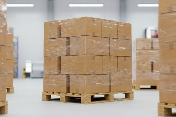 Shrink-wrapped brown cardboard master cartons stacked on a wooden pallet in a bright warehouse, optimized for CPG distribution.