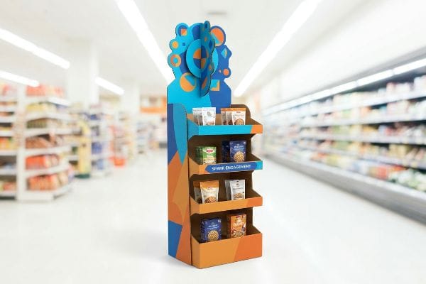 Retail end cap display with blue and orange geometric 3D die-cuts, four shelves of snacks, and 'Spark Engagement'.