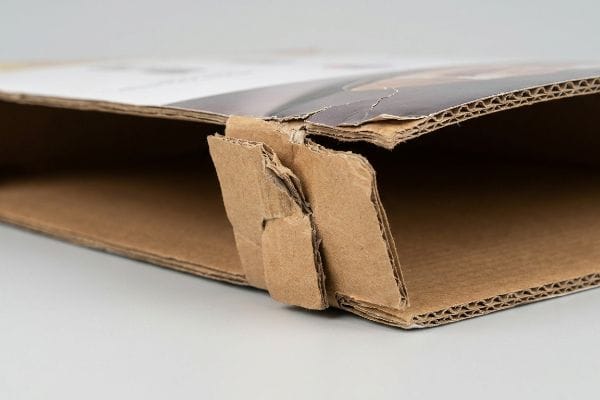 Torn corrugated cardboard joint showing swollen fibers and crushed internal flutes, highlighting humidity damage.