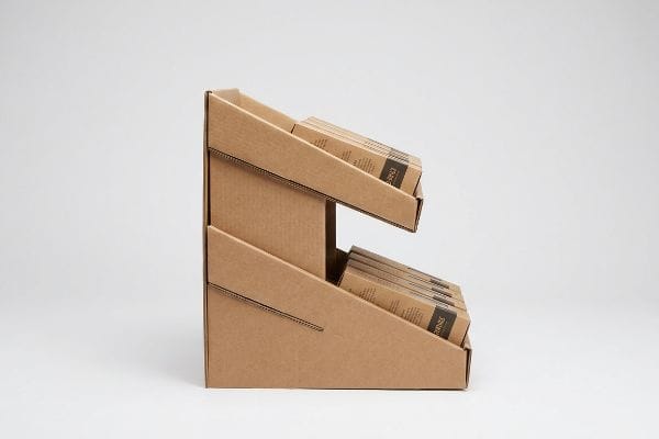 Cardboard Gravity Feed Rack Two-tiered brown corrugated cardboard gravity feed rack displaying small brown boxes with dark labels, optimizing retail merchandising.