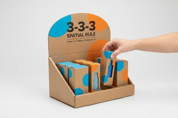 クラフト紙製のディスプレイで、3-3-3空間ルールを紹介。青いボトルを型抜きされた箱に入れる手が描かれており、「30フィートで妨害、3フィートで関与、3フィートで相互作用」というテキストが添えられている。.