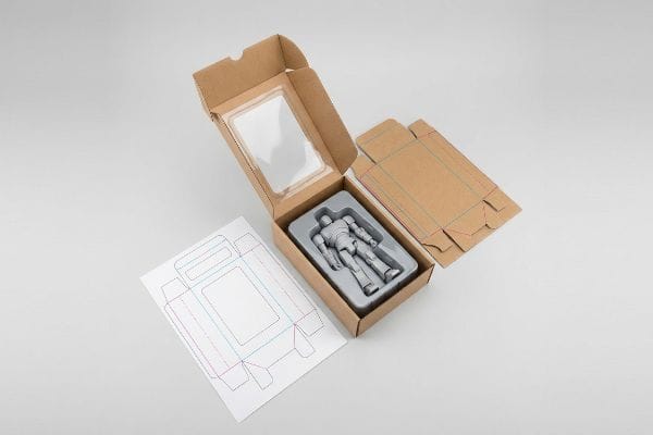 Action Figure Packaging Dielines An open brown cardboard box with a clear window showcases a gray action figure in a plastic insert, alongside flat dieline templates for custom packaging.