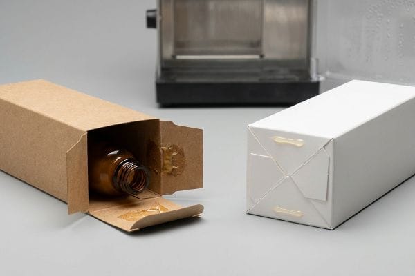 Packaging Adhesive Failure Brown kraft box with amber bottle and white packaging box, showing yellow adhesive residue from PVA glue failure.