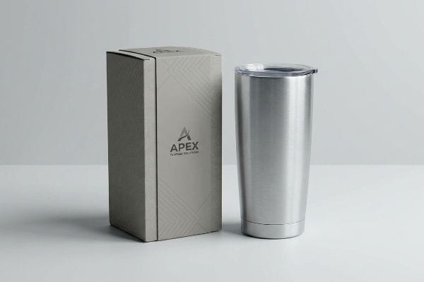 A brushed stainless steel Apex tumbler with clear lid next to its branded packaging box, featuring Apex Tumbler Solutions logo and geometric pattern.