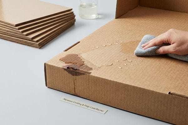 Aqueous Coating Barrier Hand wiping water from a moisture-resistant cardboard box with Aqueous Coating & Poly-Coat Barrier, showing water repellency.