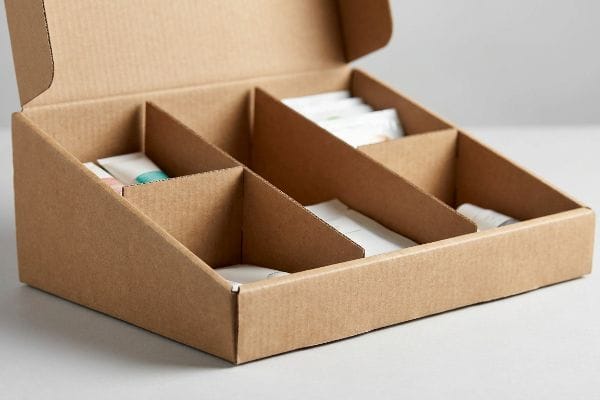 インパルスディスプレイボックス 非対称の仕切りが付いた開口部のある段ボール箱には、衝動買いを促す小売店での陳列用に設計された、小型の製品チューブやパケットが収納されている。.
