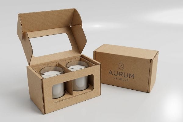 Dos cajas expositoras de velas personalizadas, de cartón corrugado marrón natural, una abierta con dos velas blancas en frascos de vidrio y una ventana recortada, junto a una caja cerrada de Aurum Candles.