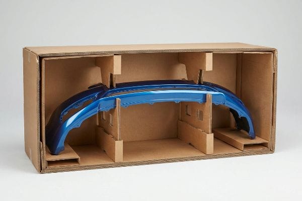 自動車用バンパーサスペンションパッケージ 段ボール製のパッケージに、特注の型抜きインサートをはめ込み、その中に鮮やかな青色の自動車用バンパーを吊り下げた。このバンパーは、運動衝撃吸収のために設計されている。.