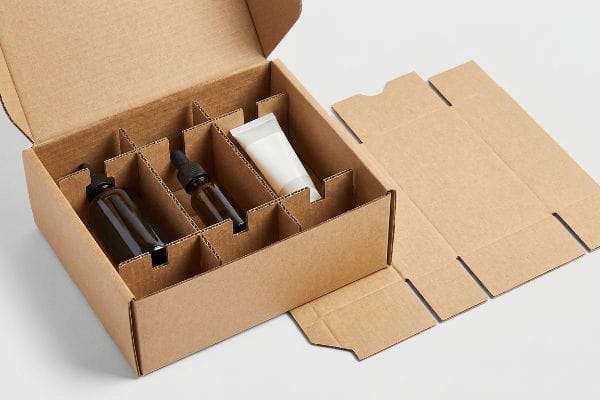 Wellness Box Dividers Natural brown corrugated cardboard box with B-flute internal dividers holding amber glass dropper bottles and a white squeeze tube for a wellness kit.