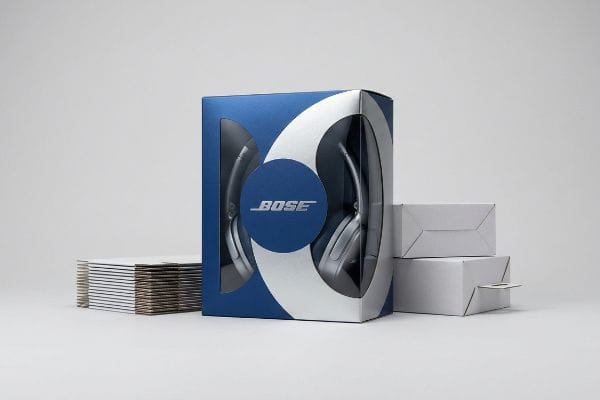 Blue and silver Bose headphones retail packaging, featuring a die-cut window, with stacked flat and assembled white shipping boxes.