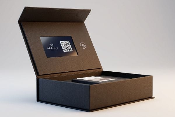 Interaktive Verpackung – Digitaler Bildschirm Die offene, schwarze interaktive Verpackungsbox verfügt über einen digitalen Bildschirm mit dem Branno-Logo und einem QR-Code sowie einem sichtbaren Lautsprechersymbol.