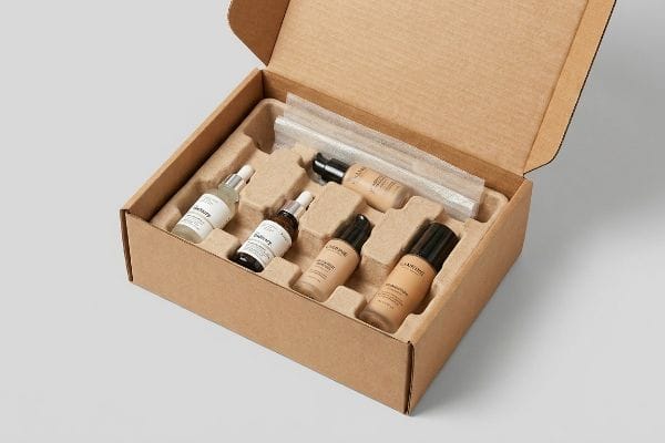 Cosmetic Shipping Box Packaging An open brown cardboard shipping box reveals a custom micro-fluted corrugated insert holding six cosmetic bottles, including The Ordinary serums and Lancôme foundations.