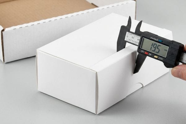 Caliper Measures Carton Dimension Digital caliper measures 19.5 mm internal dimension of a white folding carton, ensuring precise packaging tolerance.