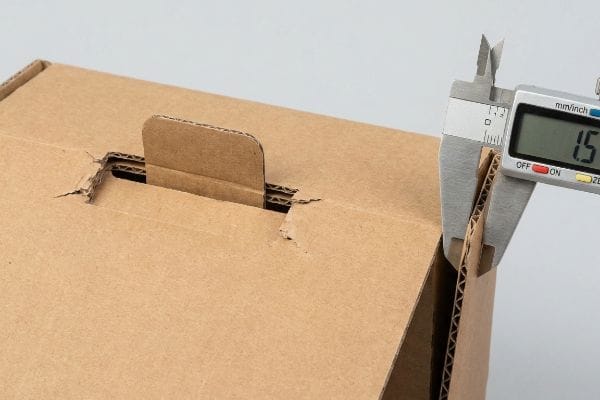 Brown corrugated cardboard box measured by a digital caliper, displaying 1.5 mm thickness for bend allowance.