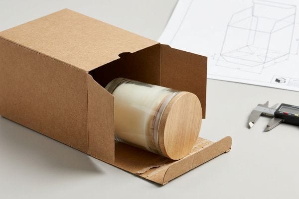 Candle Packaging Design Process Raw kraft paperboard box packaging a glass candle jar with a wooden lid, near a dieline and digital caliper.