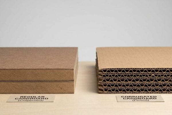 Cardboard vs Corrugated Comparison Brown stacks of Regular Cardboard (Chipboard) and Corrugated Cardboard (Fluted) side-by-side, highlighting their distinct internal structures.