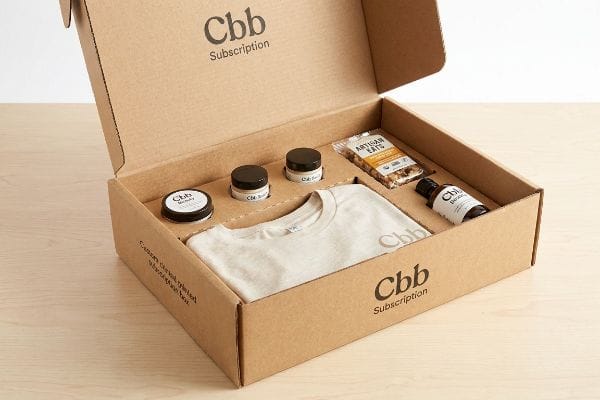 Cbb Subscription Box Contents An open Cbb subscription box with a custom corrugated insert holds a Cbb Beauty jar, Artisan Eats snack, Cbb t-shirt, and an oil dropper bottle.